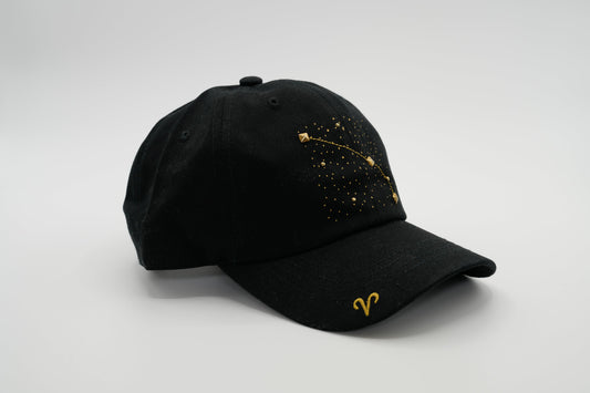 A black baseball cap with the Aris zodiac sign embroidered and riveted in gold on the front.