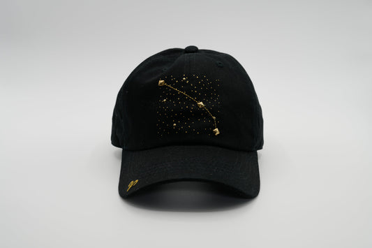 A black baseball cap with the Aris zodiac sign embroidered and riveted in gold on the front.