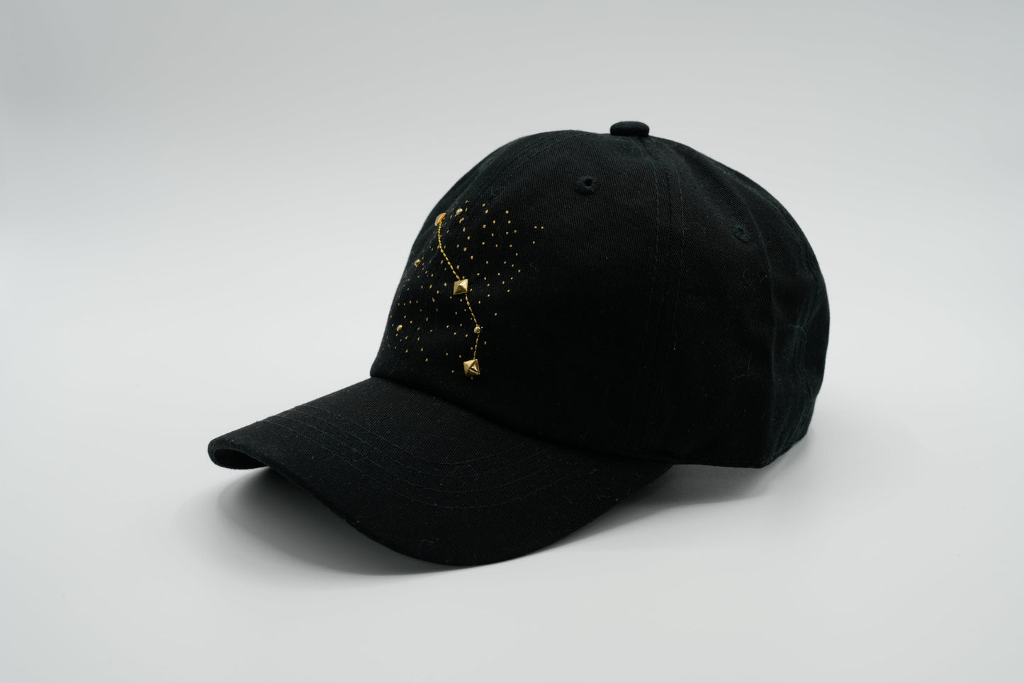 A black baseball cap with the Aris zodiac sign embroidered and riveted in gold on the front.