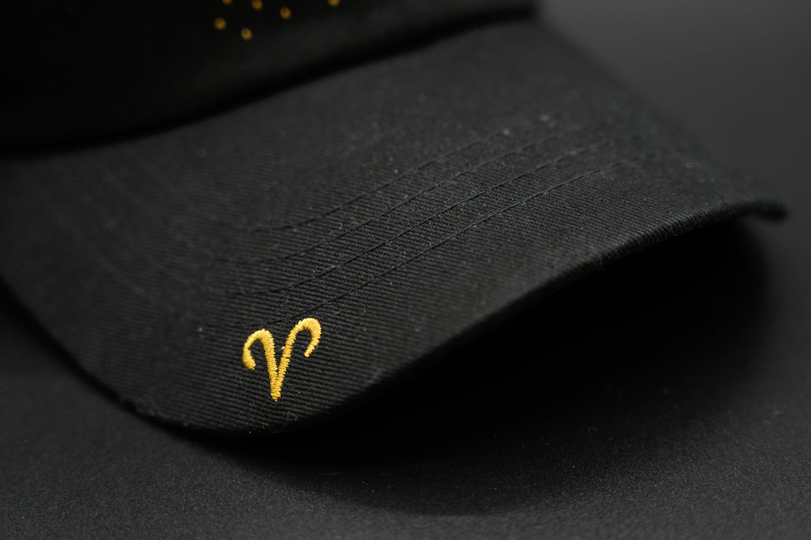 A black baseball cap with the Aris zodiac sign embroidered and riveted in gold on the front.