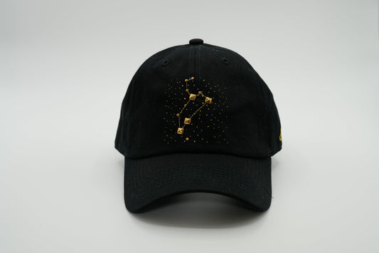 A black baseball cap with the Leo zodiac sign embroidered and riveted in gold on the front.