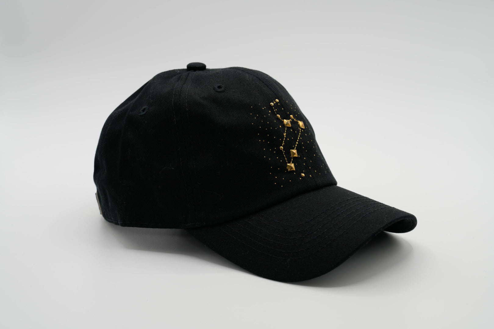 A black baseball cap with the Leo zodiac sign embroidered and riveted in gold on the front.