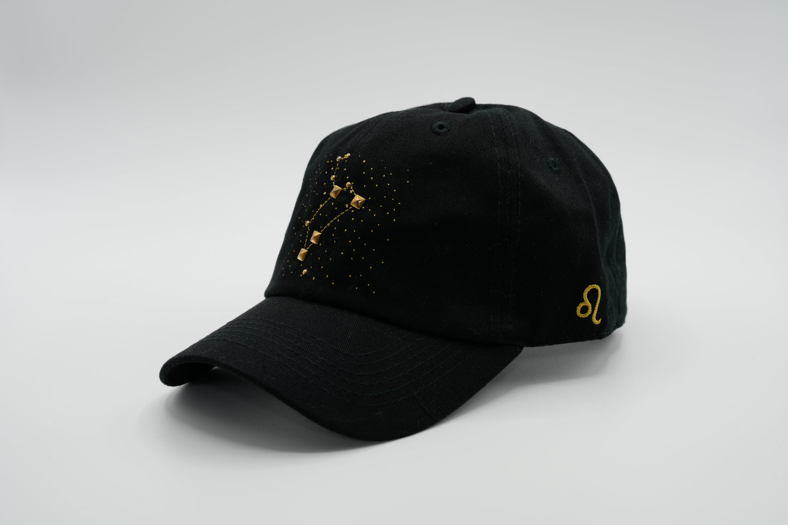 A black baseball cap with the Leo zodiac sign embroidered and riveted in gold on the front.