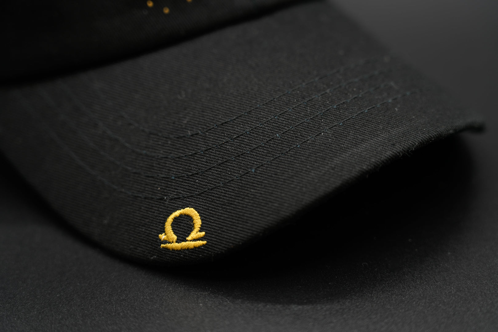 A black baseball cap with the Libra zodiac sign embroidered and riveted in gold on the front.