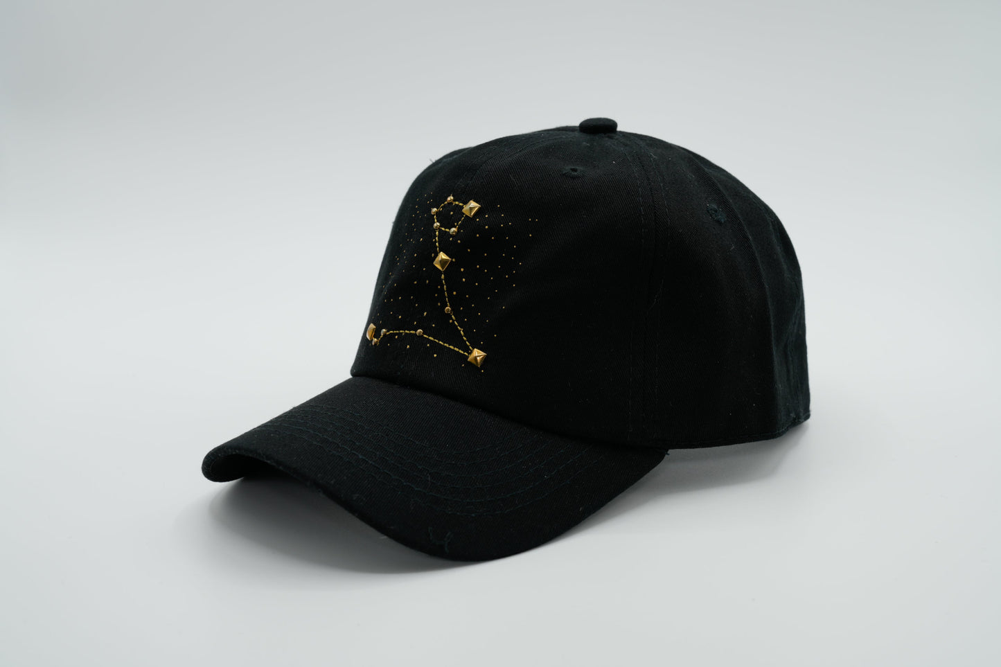 A black baseball cap with the Pisces zodiac sign embroidered and riveted in gold on the front.