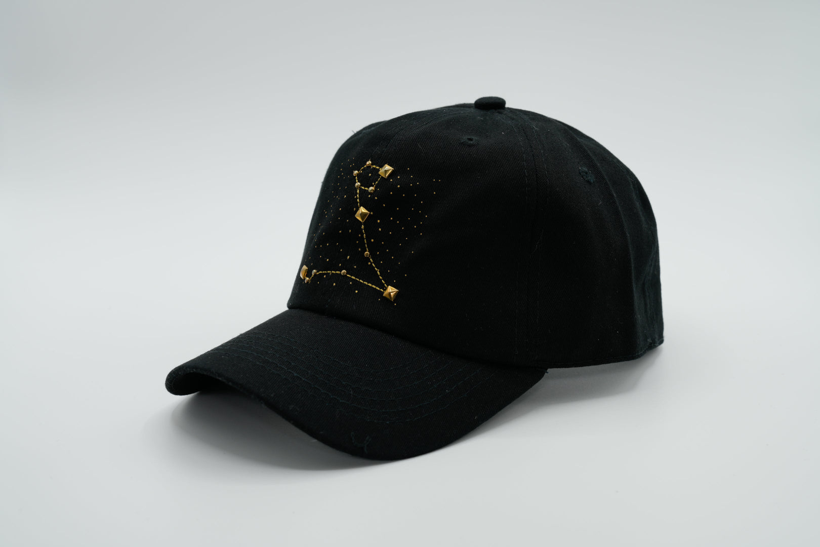 A black baseball cap with the Pisces zodiac sign embroidered and riveted in gold on the front.
