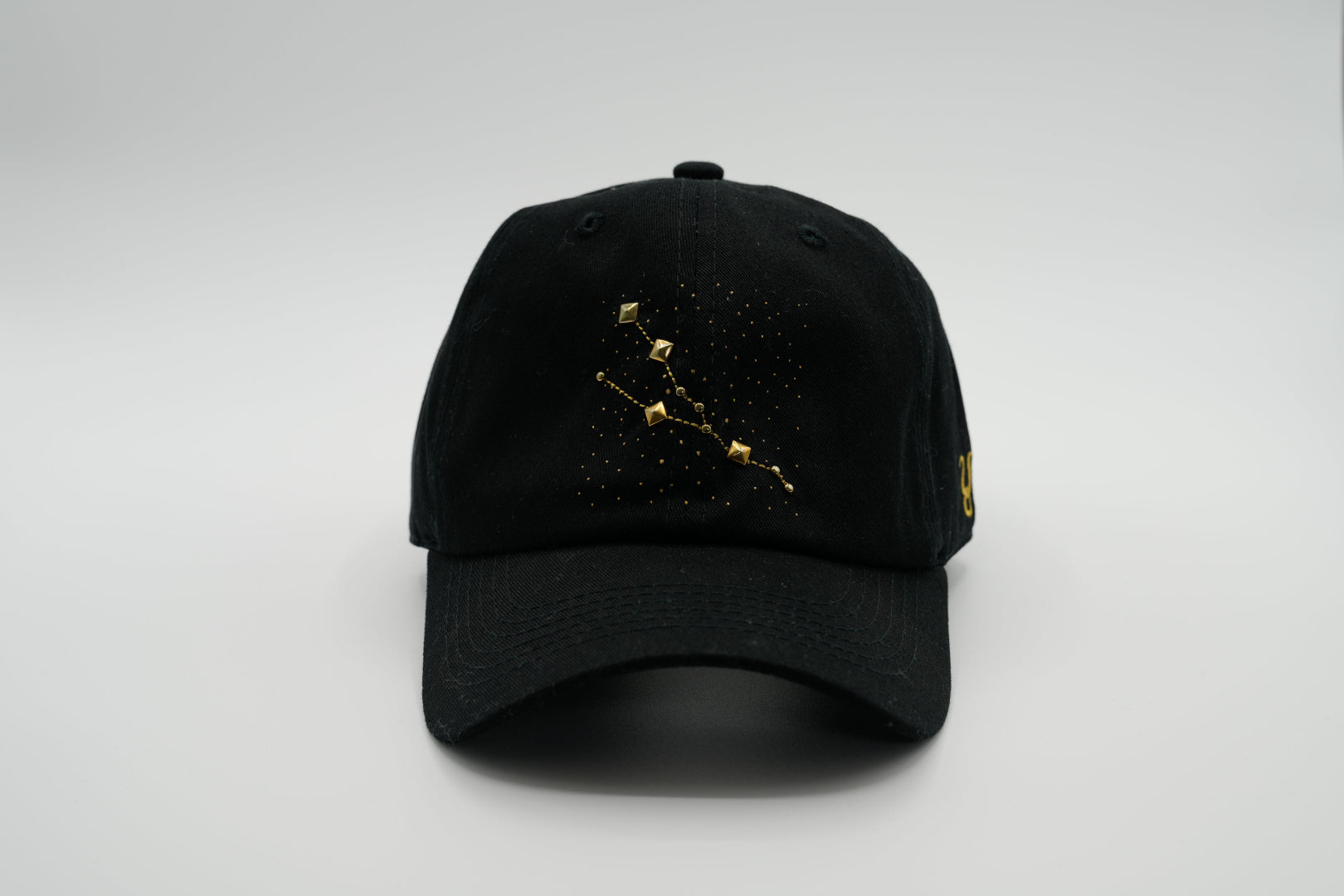 A black baseball cap with the Taurus zodiac sign embroidered and riveted in gold on the front.