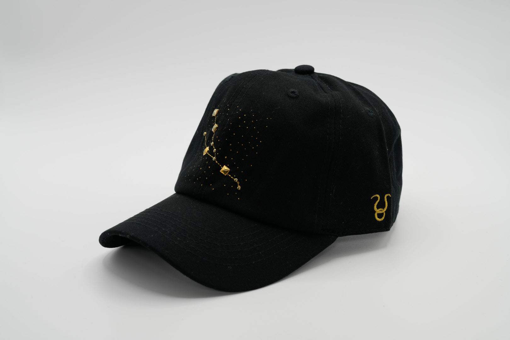 A black baseball cap with the Taurus zodiac sign embroidered and riveted in gold on the front.