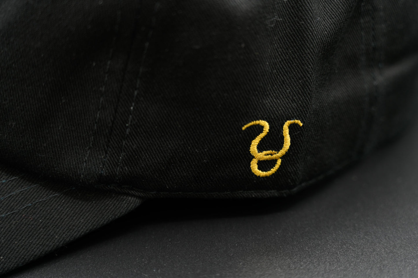 A black baseball cap with the Taurus zodiac sign embroidered and riveted in gold on the front.