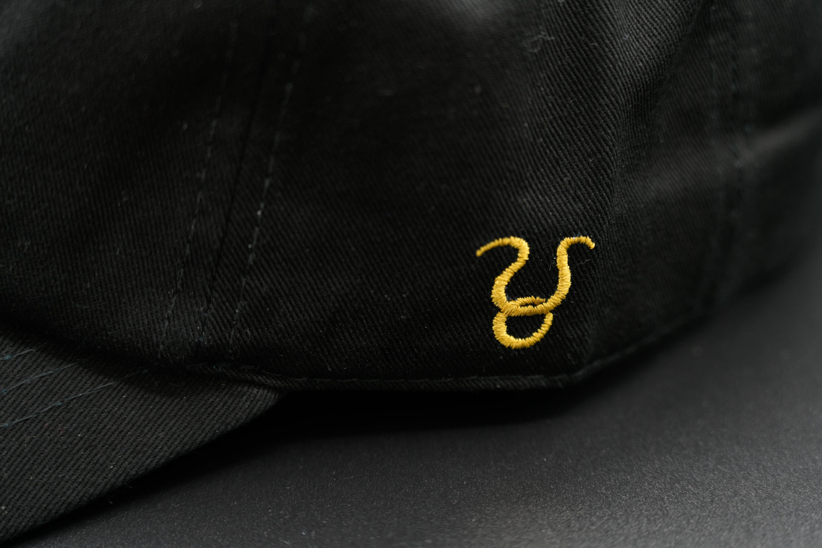 A black baseball cap with the Taurus zodiac sign embroidered and riveted in gold on the front.